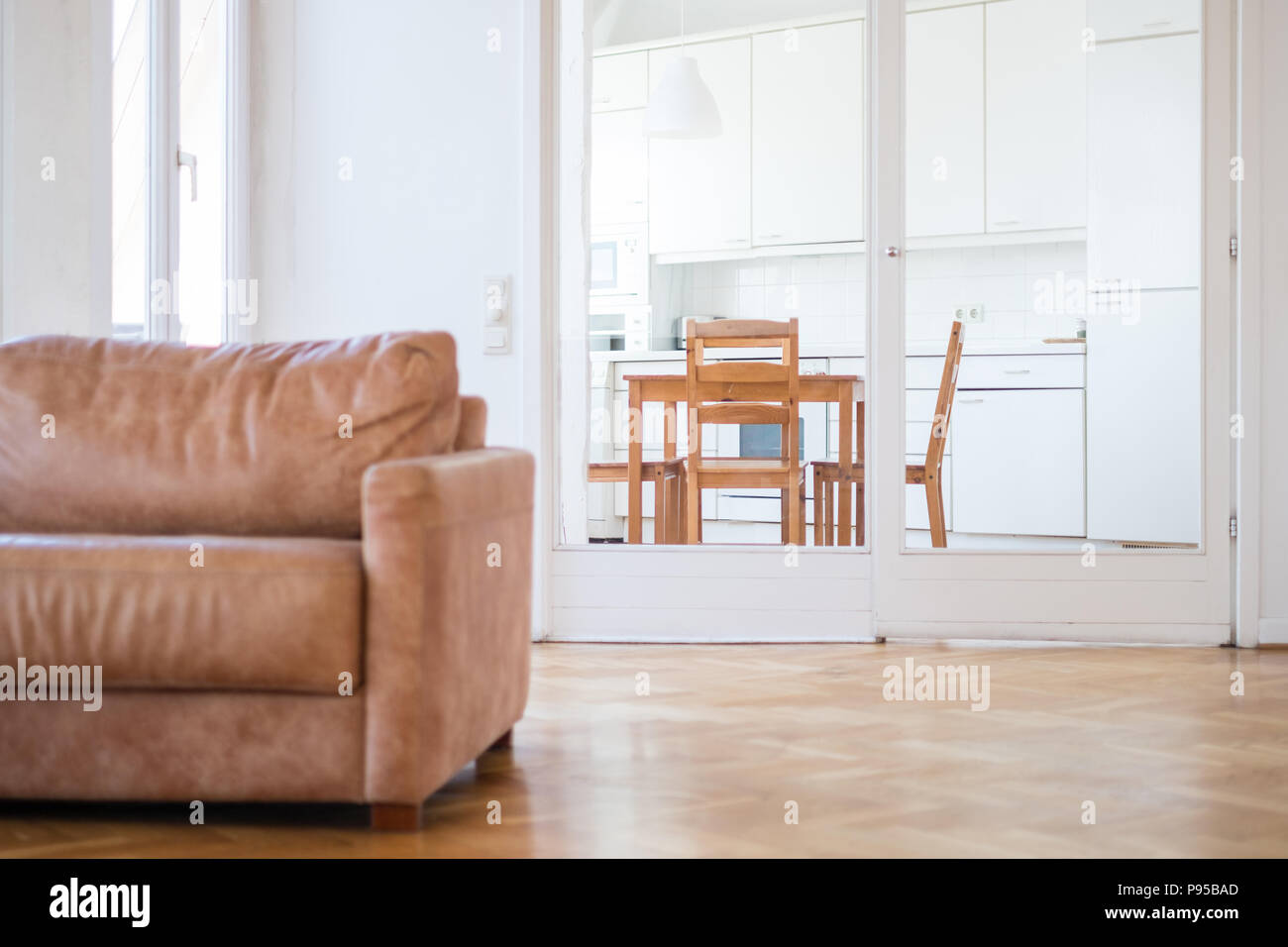 Appartamento interno di un soggiorno con pavimento in legno e un divano e cucina in background Foto Stock