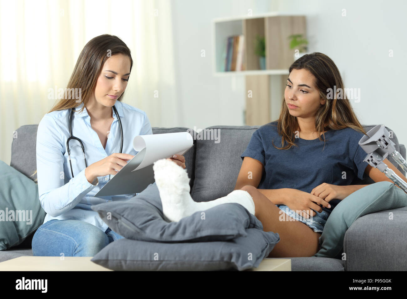 Il medico e il paziente controllando la storia medica seduto su un divano nel salotto di casa Foto Stock