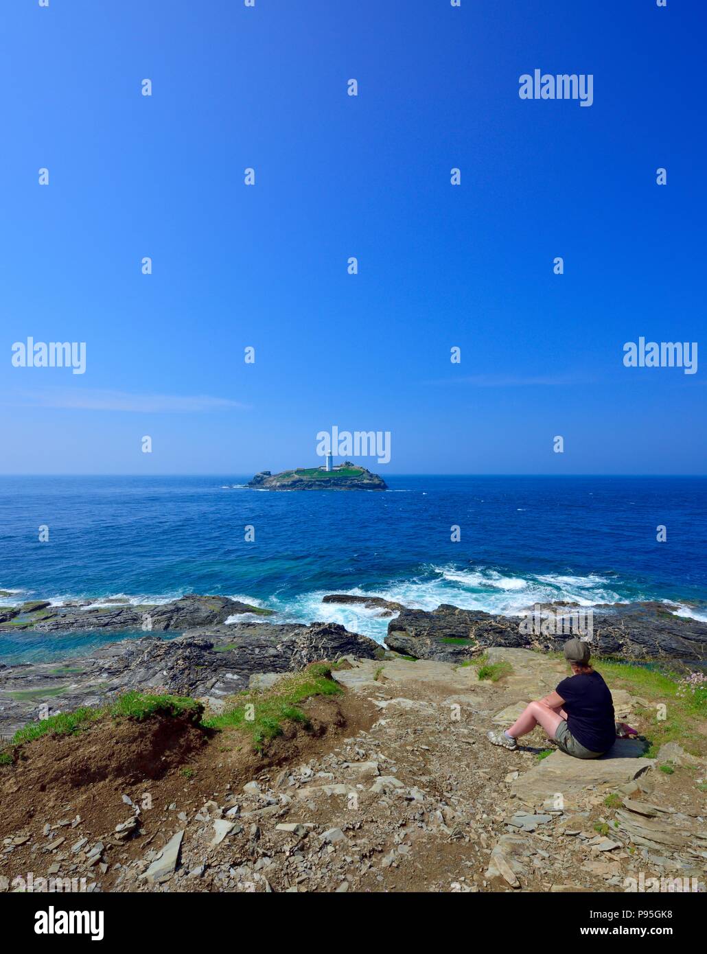 Turista femminile seduto a guardare fuori verso Godrevy lighthouse,Gwithian Godrevy,Costa del patrimonio,Cornwall,l'Inghilterra,UK Foto Stock