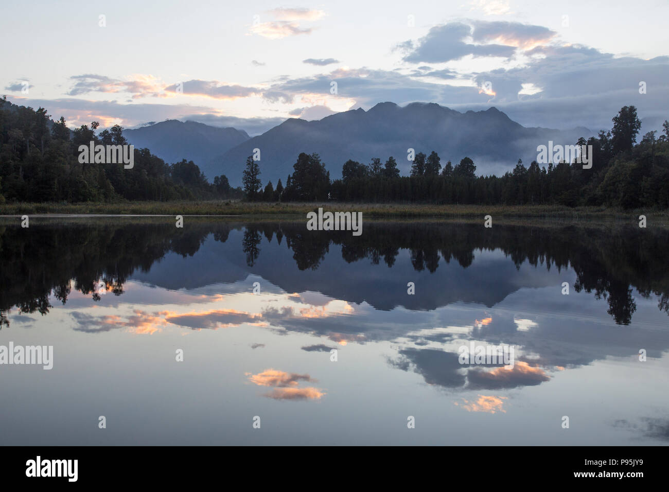 Alberi e montagne che si riflettono su ancora un lago, lago Matheson, Nuova Zelanda Foto Stock