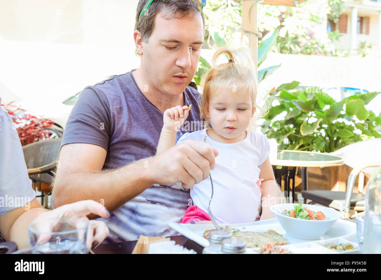 Padre adulto alimentando il suo simpatico bimbo figlia durante la family colazione in caffetteria all'esterno. Il riposo della famiglia, di trascorrere del tempo insieme concetto. Tradizioni di famiglia Foto Stock