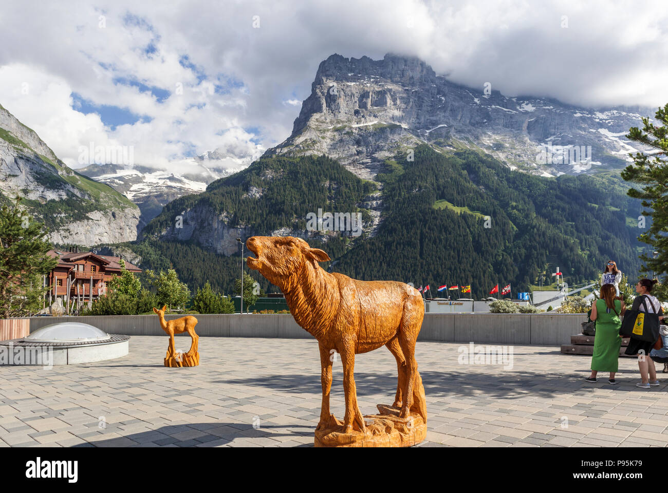 Legno scolpito la Statua di una mucca nel centro di Grindelwald, un popolare villaggio resort per vacanze Oberland bernese con il Monte Eiger in background Foto Stock