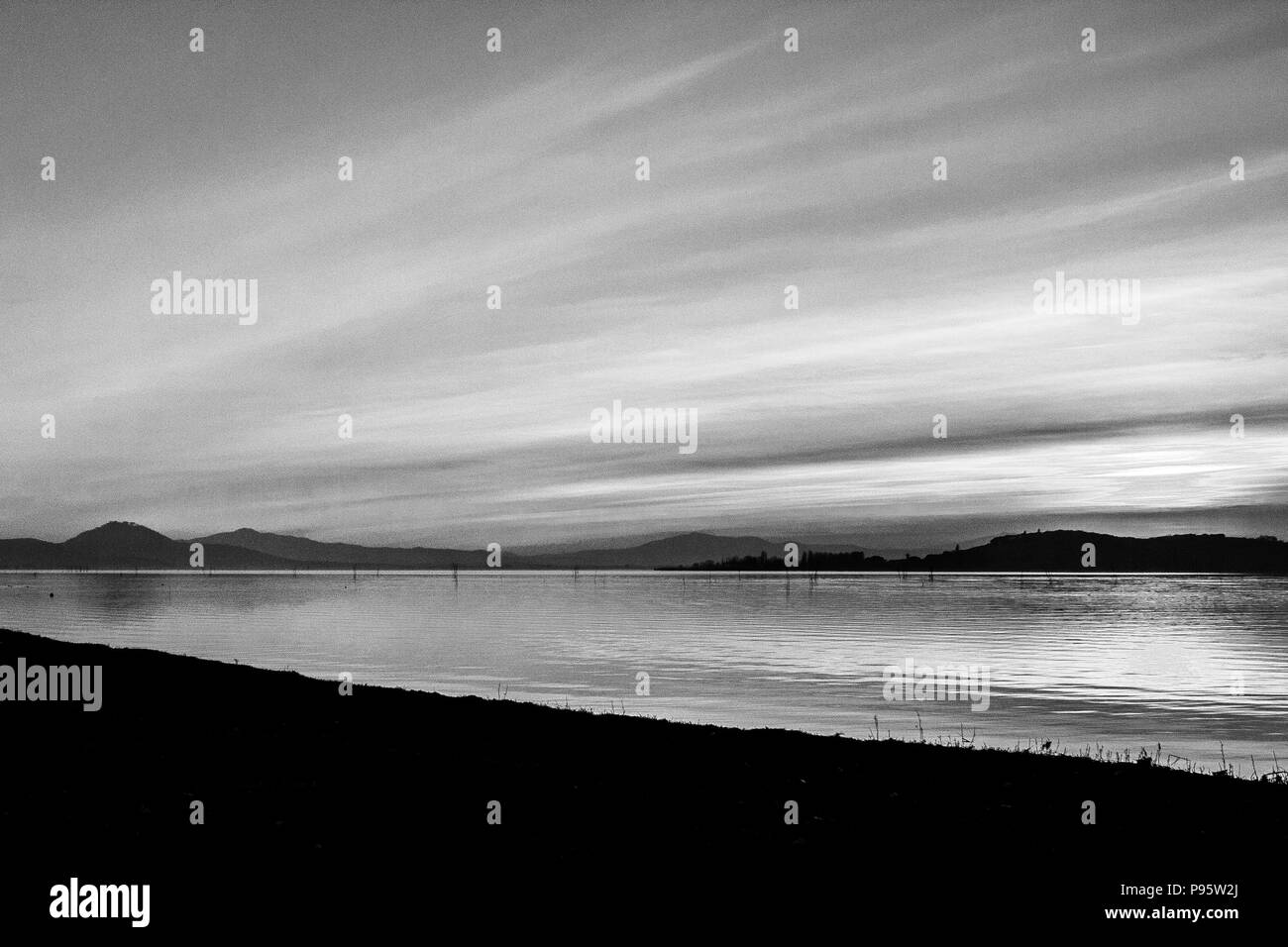 Una ripresa di un tramonto su un lago, con il sole che scende dietro e isola e molte linee diagonali creato da nuvole e onde di acqua Foto Stock