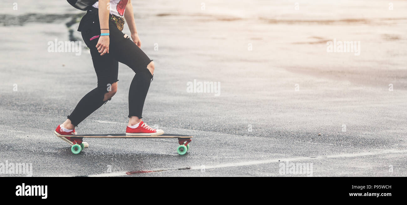 Ragazza con i jeans strappati e red sneakers longbord equitazione sulla strada Foto Stock