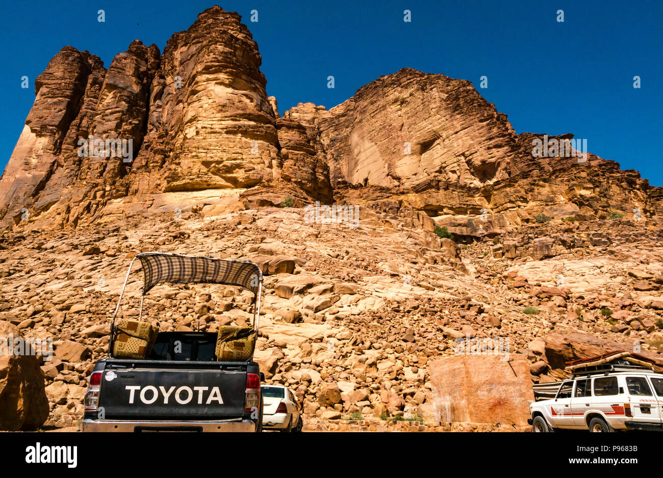 Accampamento Beduino sotto le scogliere con Toyota e 4 x4 veicoli parcheggiati, Wadi Rum vallata desertica, Giordania, Medio Oriente Foto Stock
