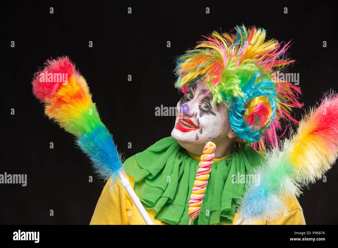 Scary clown con colorati mohawk e un sorriso con un lecca-lecca su sfondo nero Foto Stock