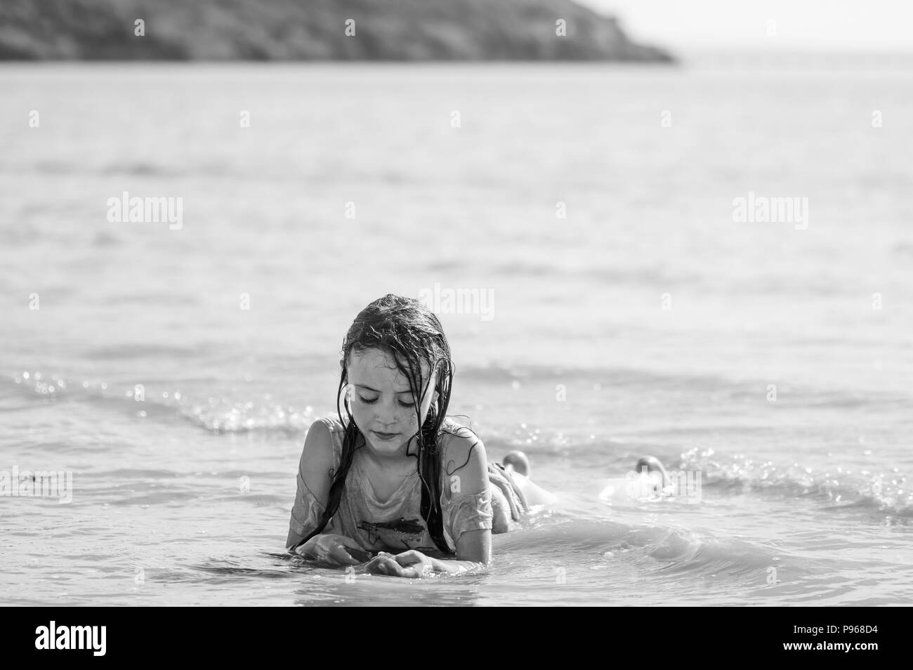 Bambino giacente in surf in bianco e nero. Ragazza giovane giocando in mare, persa nel suo propri pensieri Foto Stock
