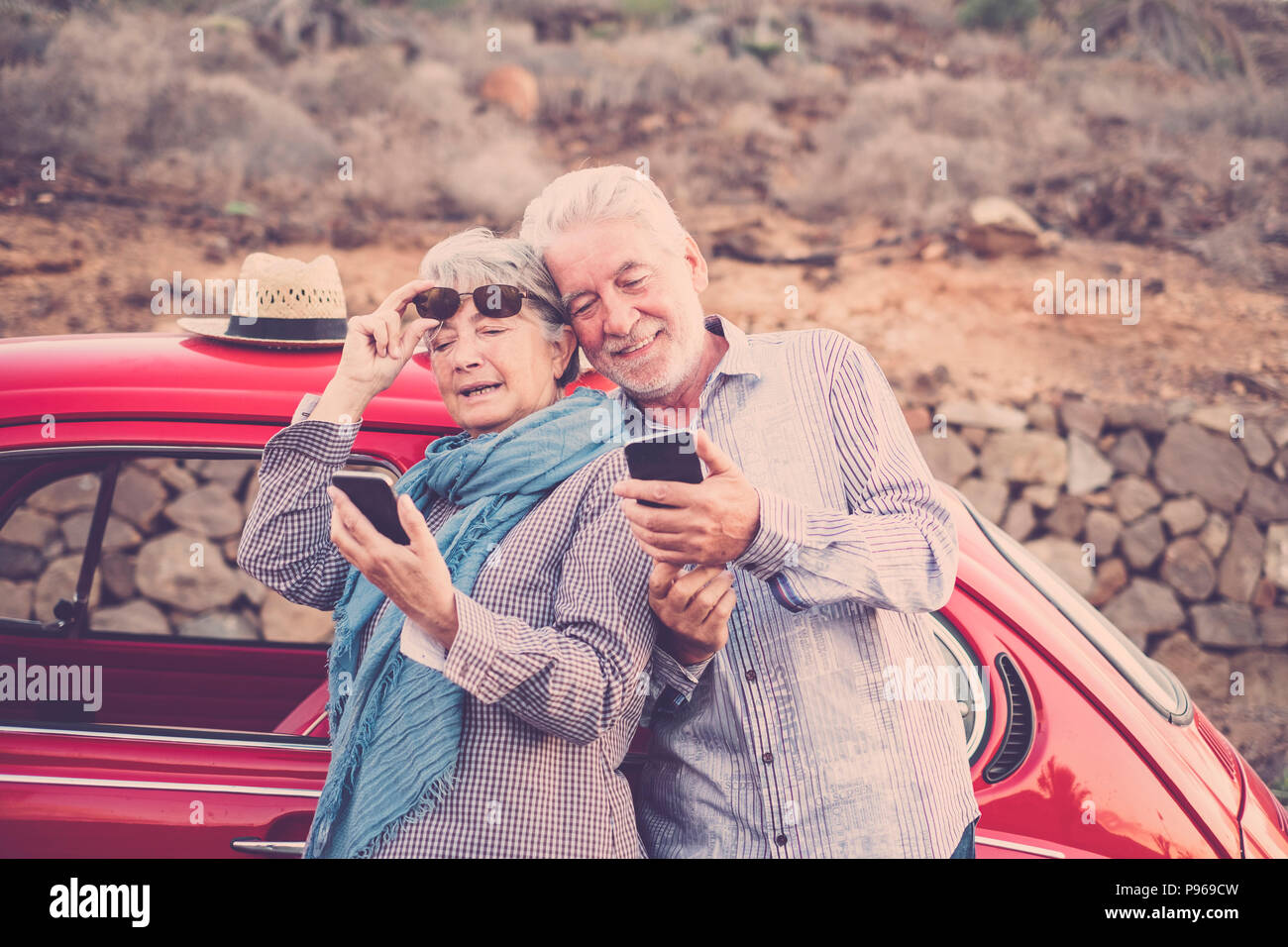 Senior adulto giovane controllare e guardare i telefoni cellulari per connettersi con internet o scattare una foto selfie. vintage auto rossa pronto a viaggiare ovunque in th Foto Stock