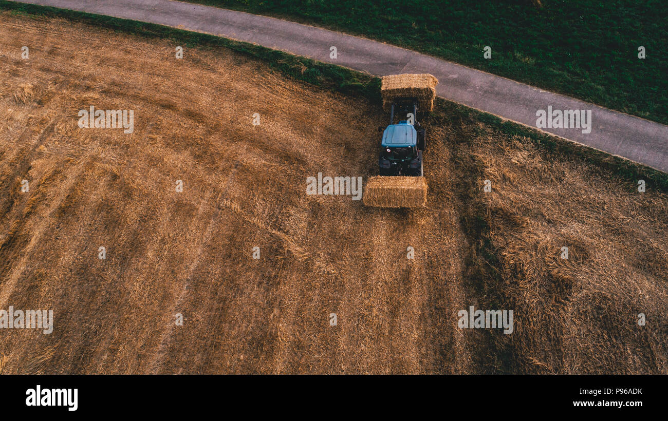 Vista aerea del campo di raccolto con il trattore in movimento della balla di fieno attorno a parte superiore verso il basso Foto Stock