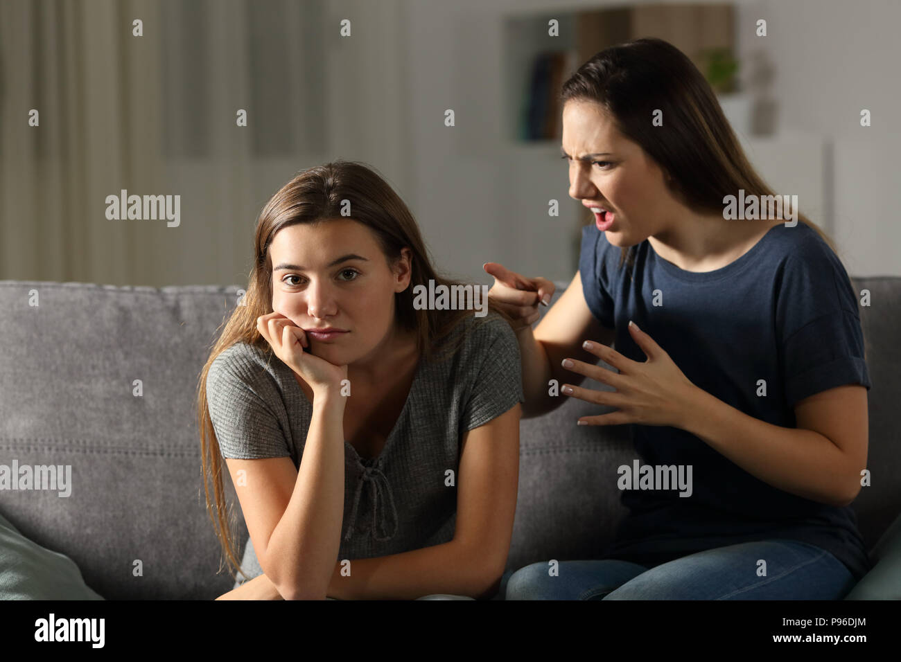 Donna scolding il suo amico chi sta guardando la telecamera seduta su un divano nel salotto di casa Foto Stock