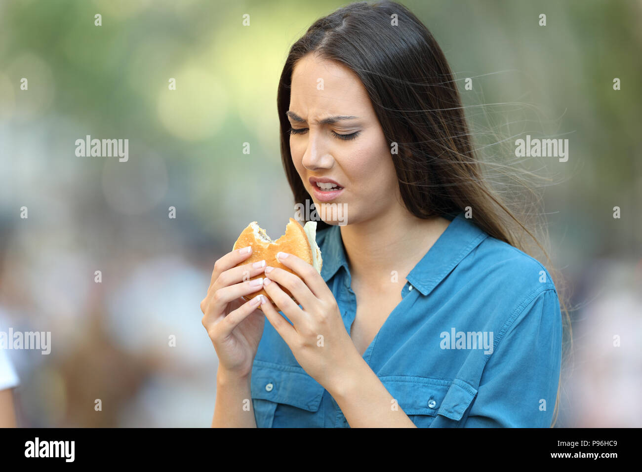 Disgustato donna mangiare un hamburger con cattivo gusto sulla strada Foto Stock