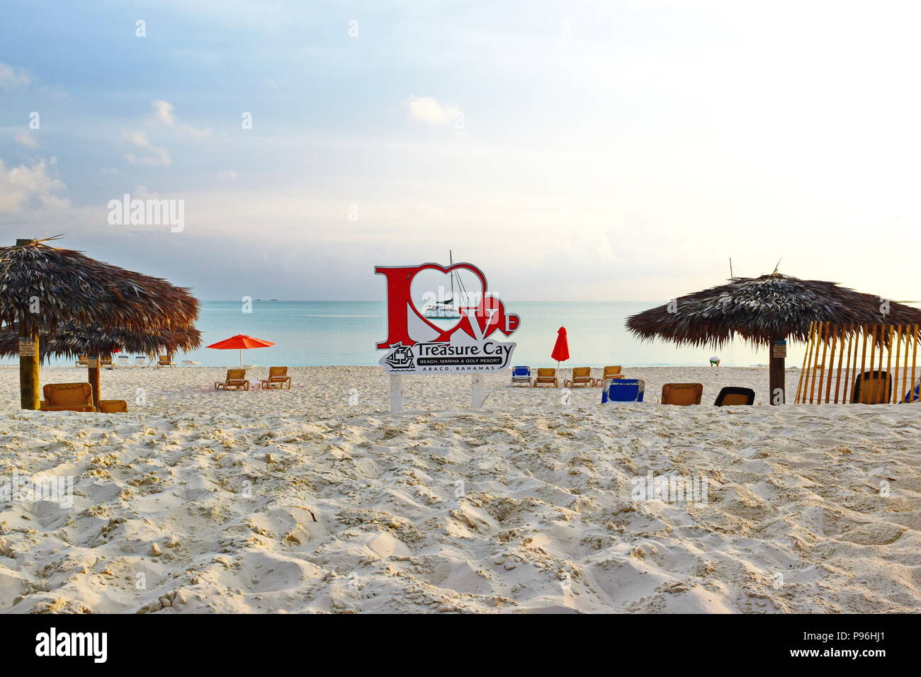 Amore Treasure Cay segno sulla spiaggia di mattina, nessun popolo. Barca in background, sedie a sdraio e ombrelloni tiki. Foto Stock