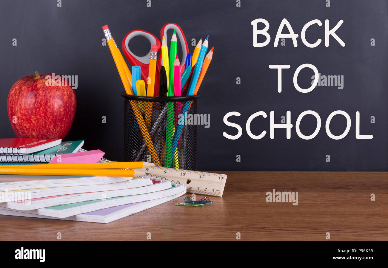 Si torna a scuola il testo scritto su una lavagna con forniture scolastiche su una scrivania in legno Foto Stock