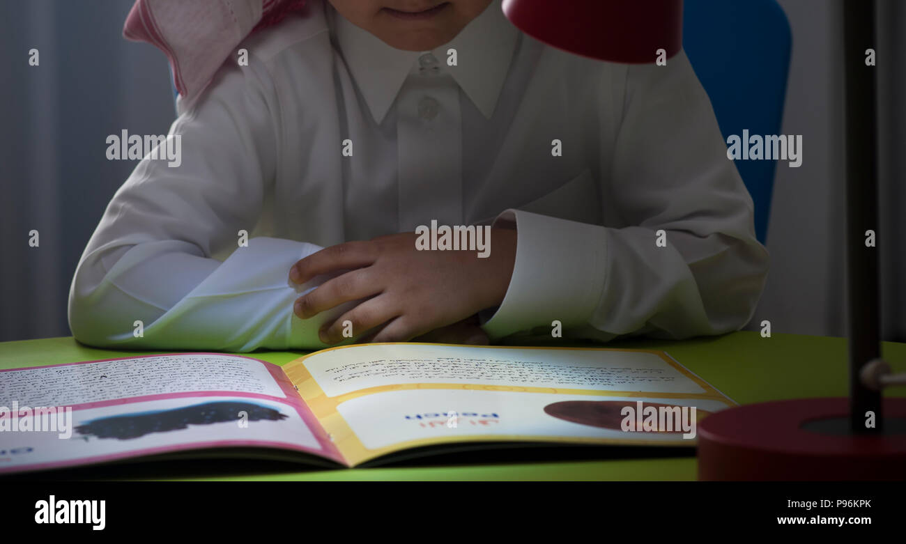 Arabia ragazzo lettura un racconto a un tavolo con lampada da vicino Foto Stock
