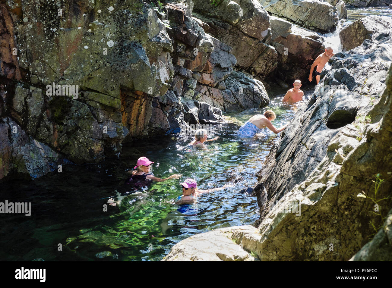 Persone wild nuoto in una piscina rocciosa in Langstrath Beck in un caldo giorno d'estate. Borrowdale Stonethwaite Parco Nazionale del Distretto dei Laghi Cumbria Inghilterra England Regno Unito Foto Stock