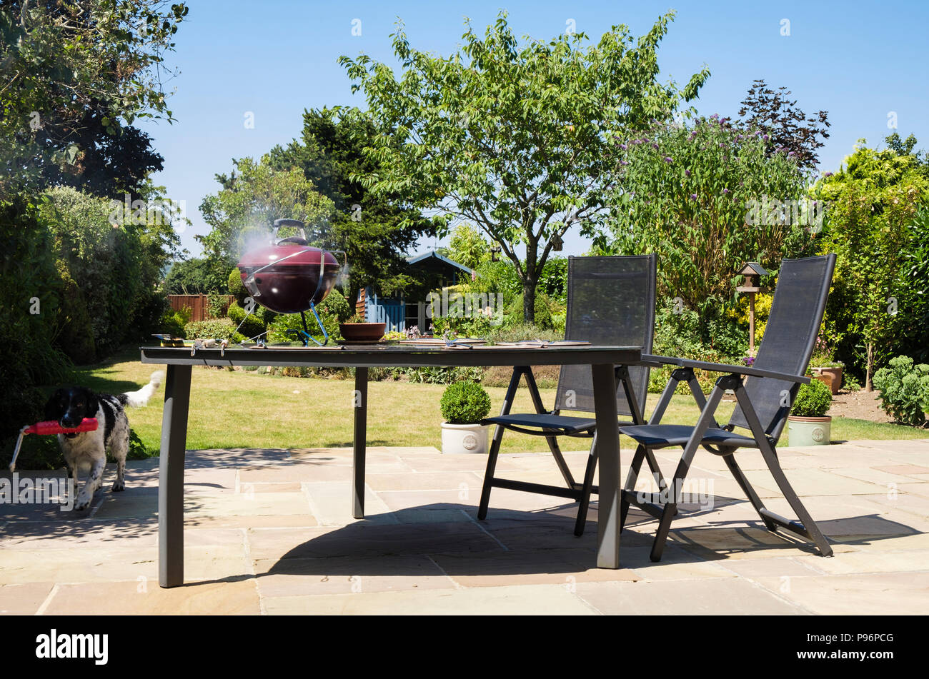 Fumatori barbecue su un tavolo da picnic in un domestico retro giardino d'estate. Kent, Inghilterra, Regno Unito, Gran Bretagna Foto Stock