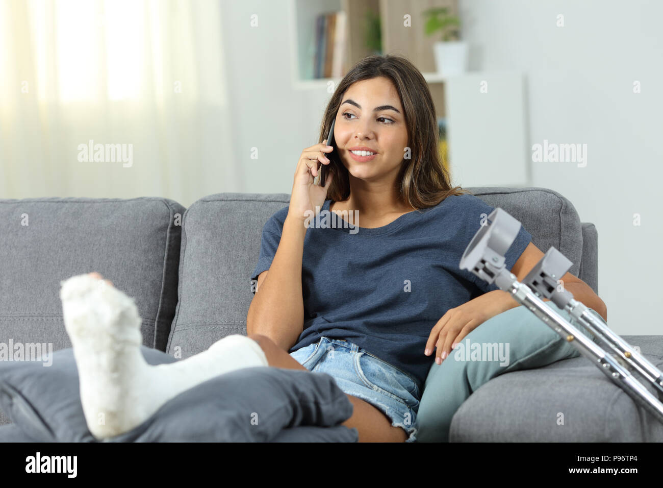 Donna disabile parlando al telefono seduto su un divano nel salotto di casa Foto Stock