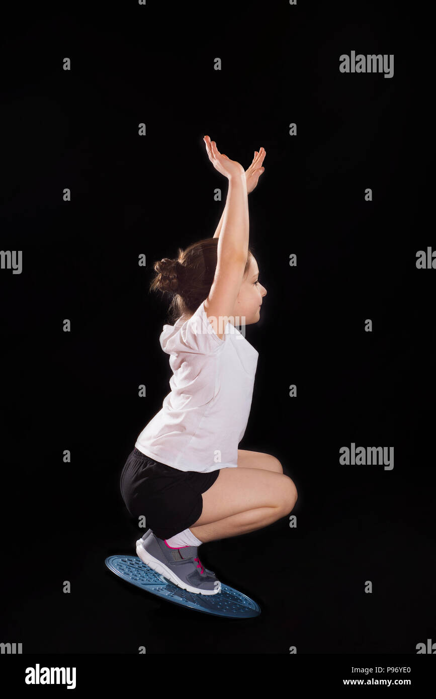 Piccola ragazza caucasica facendo squat su balance board Foto Stock