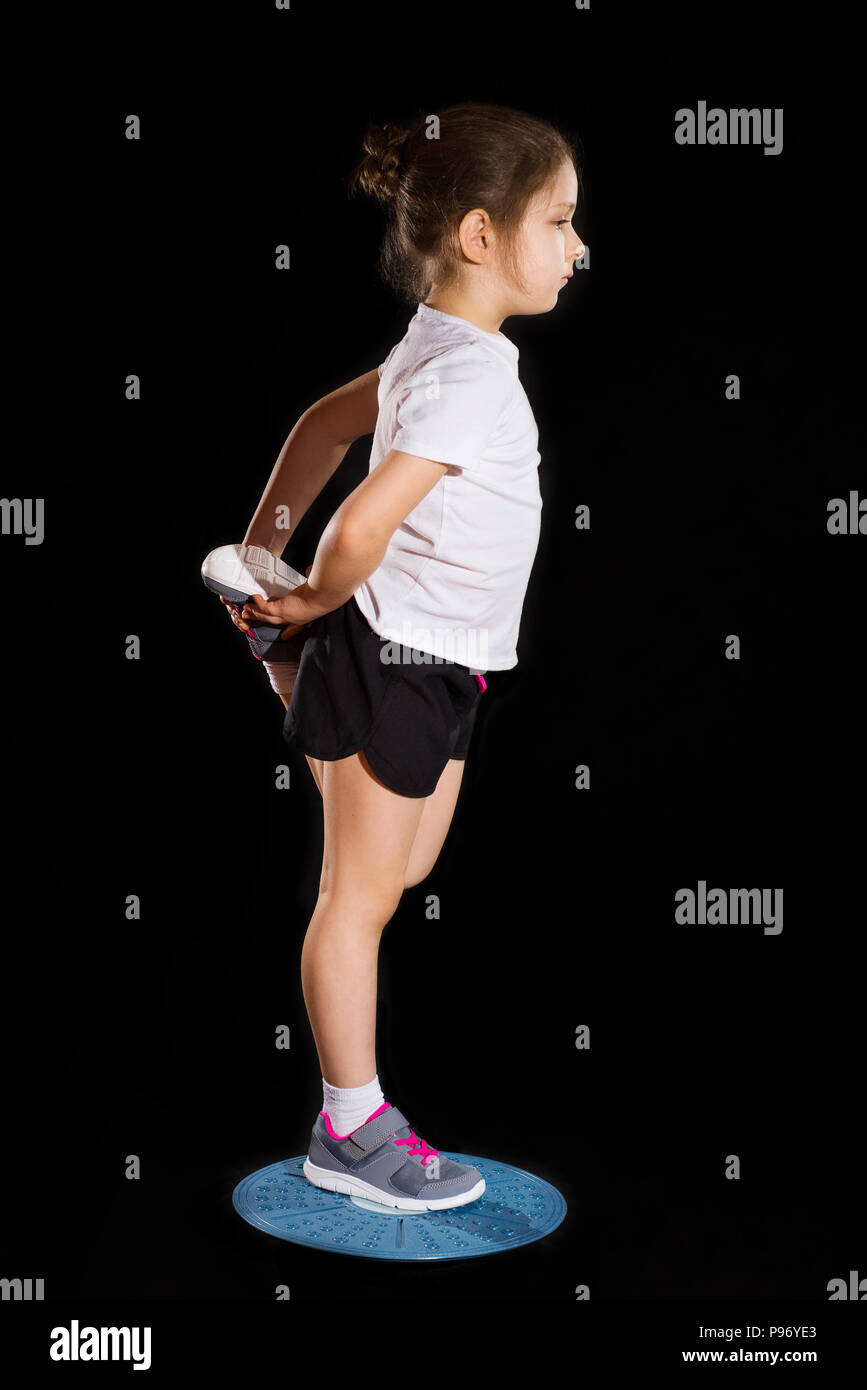 Piccola ragazza caucasica in su una gamba sola posizione su balance board Foto Stock