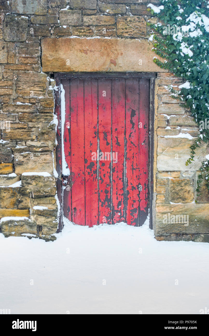 Vecchio rosso porta in un muro di pietra con neve sul terreno Foto Stock