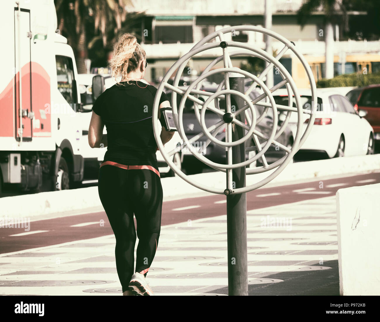 Vista posteriore della femmina/donna pareggiatore di ascolto di musica durante il jogging al fianco di città trafficata strada. Foto Stock