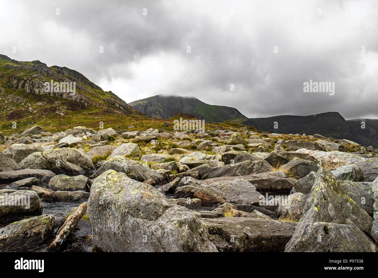 In corrispondenza del bordo roccioso di un lago di montagna cercando su-reparti al cloud coperti picchi. Foto Stock