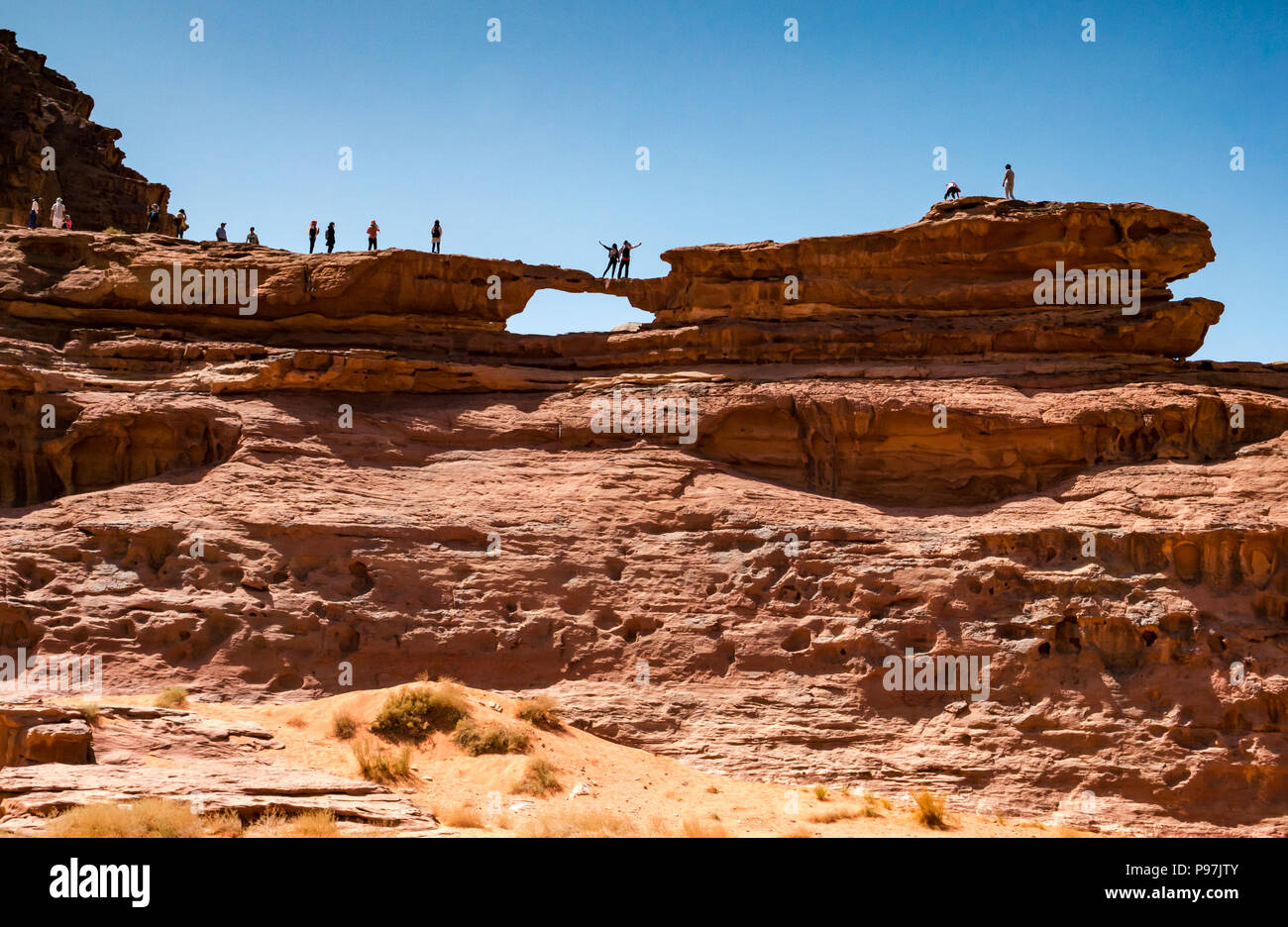 I turisti che posano per una fotografia in piedi su un enorme arco naturale di roccia, ponte Wadi Rum vallata desertica, Giordania, Medio Oriente Foto Stock