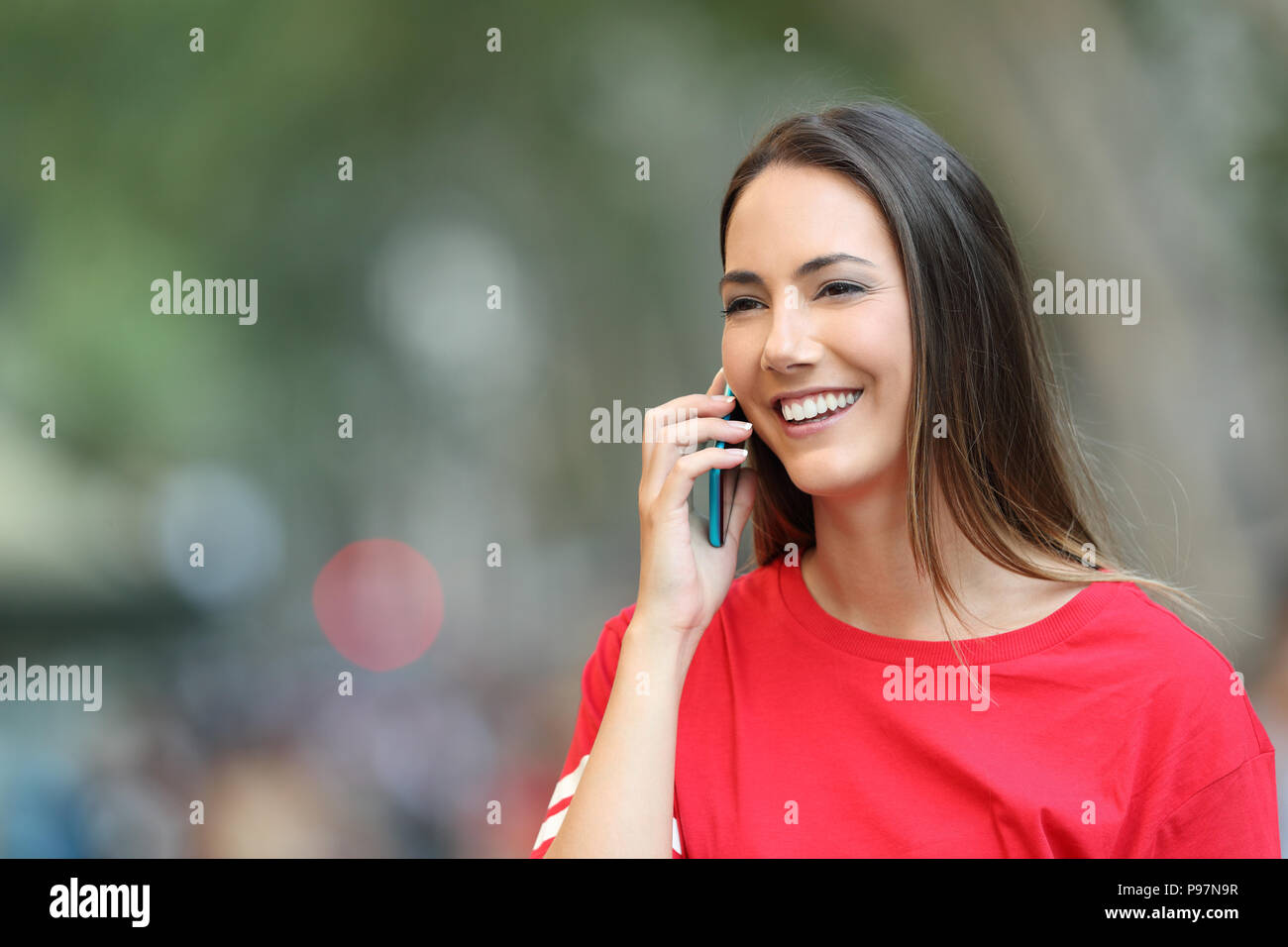 Felice ragazza in rosso parla al telefono e passeggiate sulla strada guardando lontano Foto Stock