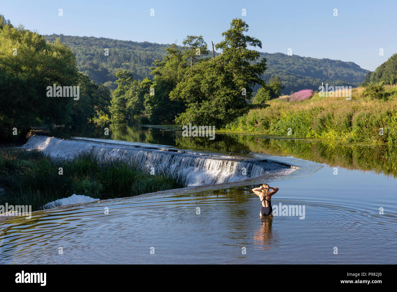 Un nuotatore in piedi in fondali bassi la preparazione di nuotare nel fiume Avon a Warleigh Weir nel Somerset, Inghilterra Foto Stock