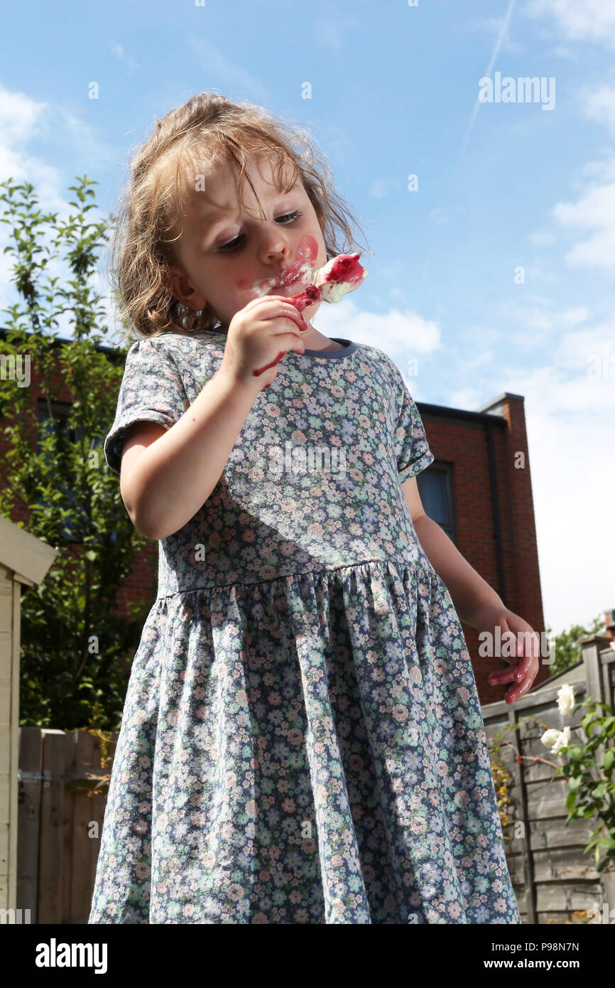 Una giovane ragazza raffigurato in un giardino godendo di un gelato sotto il sole a Londra, Regno Unito. Foto Stock