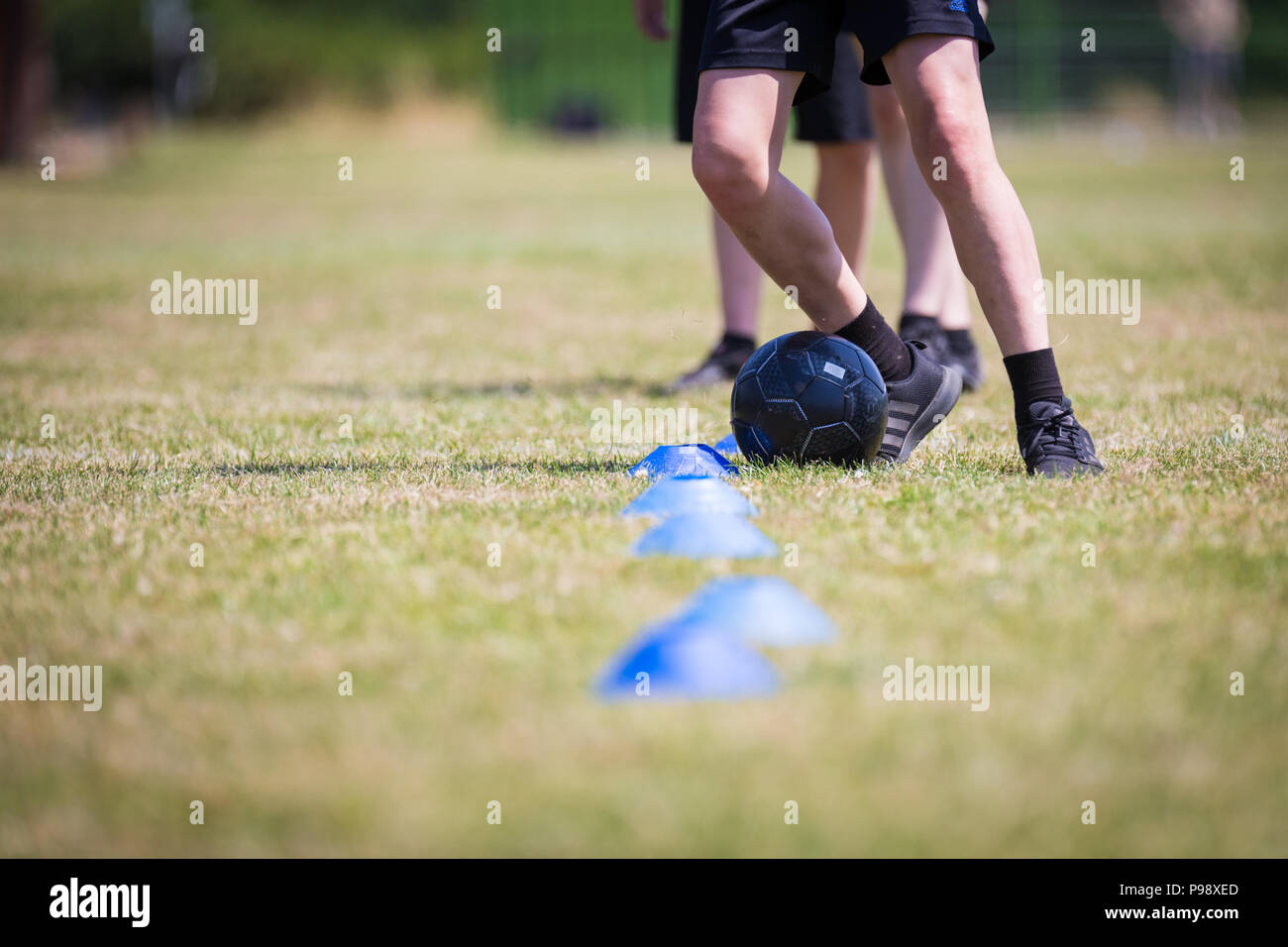 Tre scolari praticando football soccer le competenze in un campo di gioco UK Foto Stock