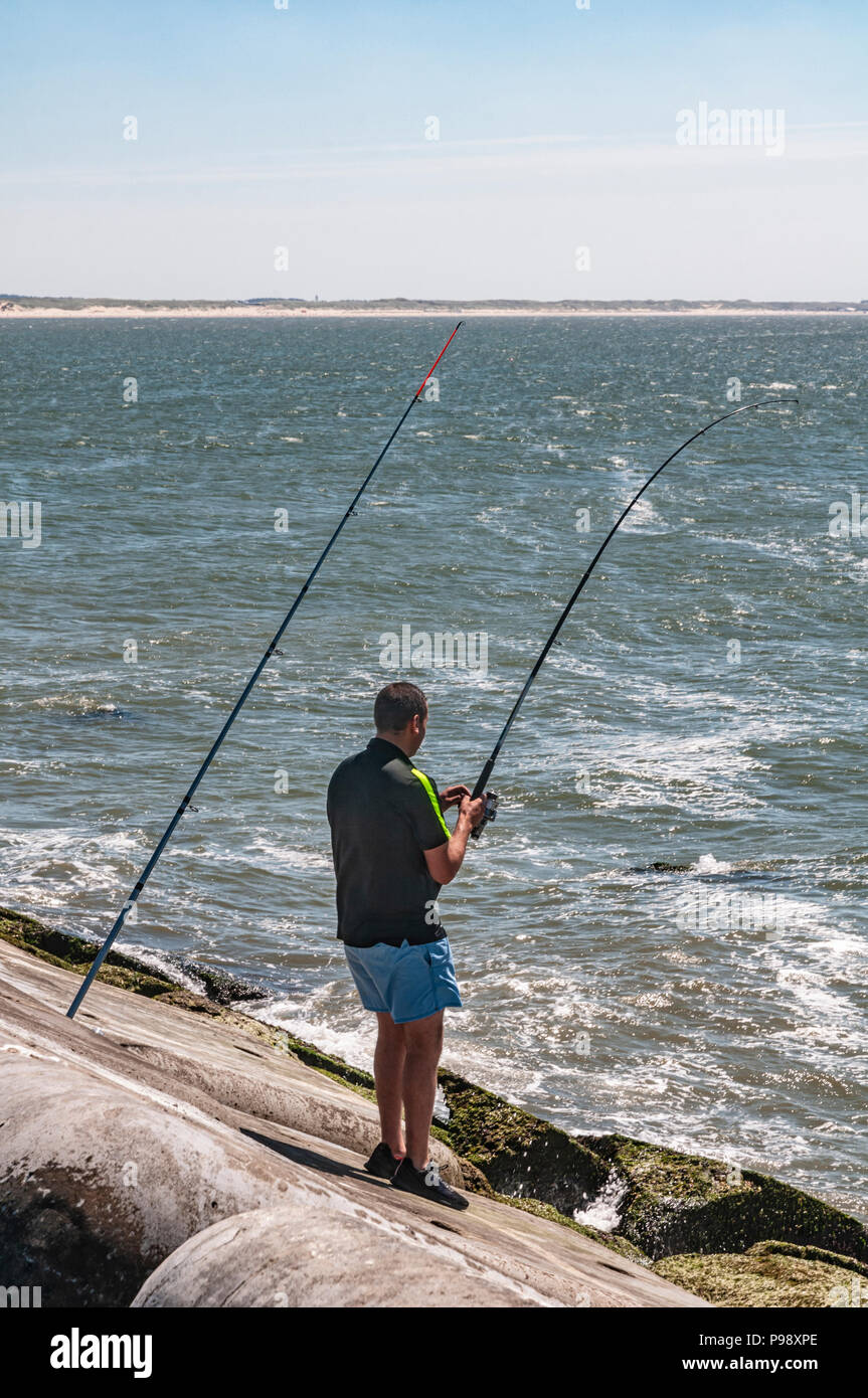 L uomo è angolato in piedi su un masso sul mare con una canna da pesca in mano Foto Stock