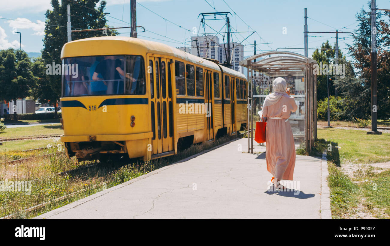 Una donna cammina a bordo di un giallo di Tatra T3 tramcar ad una fermata del tram si trova alla periferia di Sarajevo, Bosnia ed Erzegovina Foto Stock