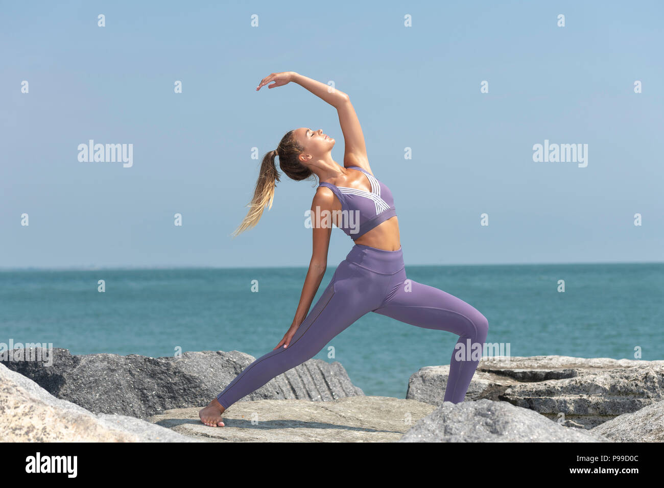 La donna a praticare yoga sulle rocce in riva al mare al sole Foto Stock
