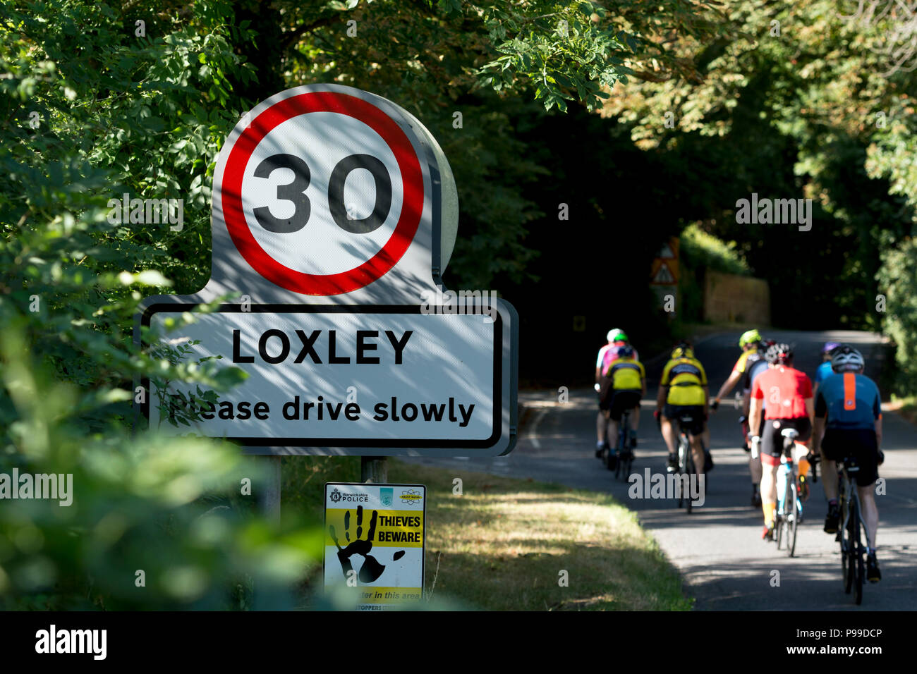 Un gruppo di ciclisti passando Loxley village segno, Warwickshire, Inghilterra, Regno Unito Foto Stock