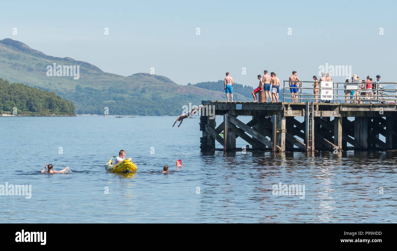 Giovani godendo un insolitamente calda giornata a Luss, Loch Lomond - nuoto, canoa e immersioni subacquee al molo durante il mese di giugno/luglio 2018 canicola Foto Stock