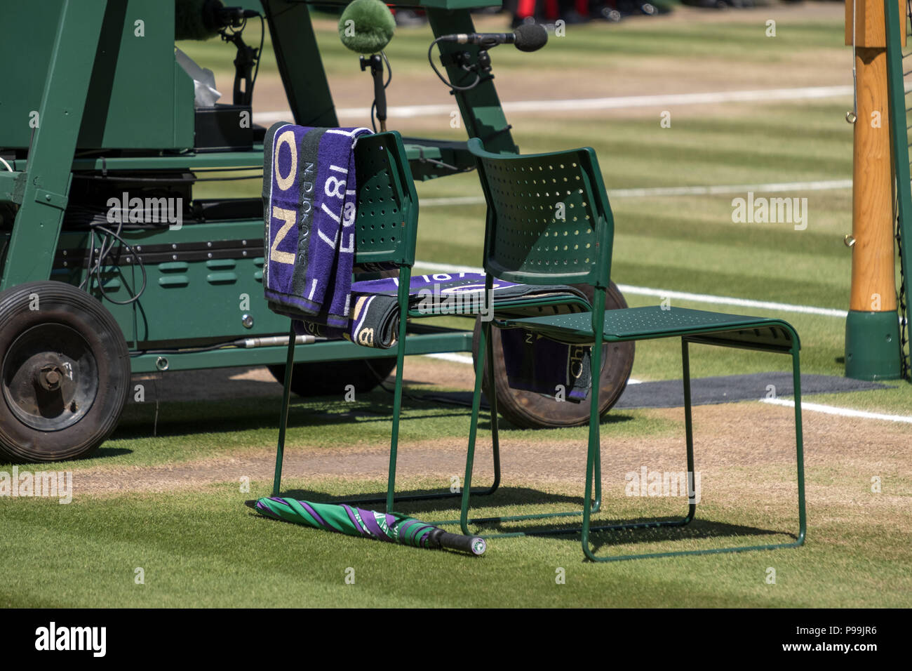 Giocatori' sedie con asciugamano piegato sul retro e una verde e viola ombrello sul terreno. Asciugamano ha il nome di Djokovic su di esso. Foto Stock