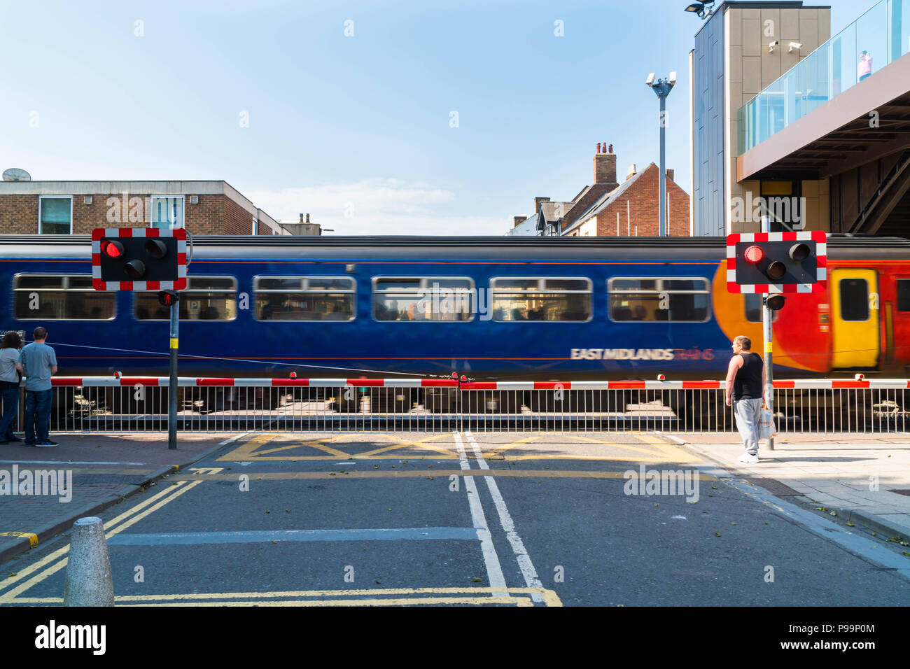Pedoni in attesa ad alto livello strada attraversando come East Midlands treno passa attraverso Lincoln UK Maggio 2018 Foto Stock