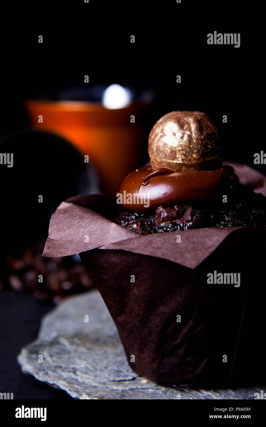 Muffin al cioccolato e rabboccato con superficie liscia di glassa di cioccolato e oro artigianale di pasticceria e presentati su un Cornish ardesia Foto Stock