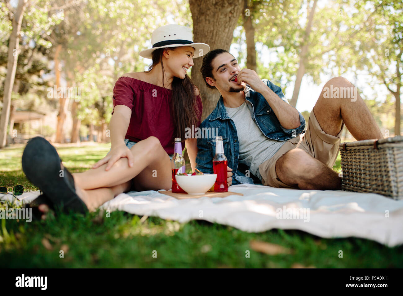 Coppia caucasica godendo una giornata al parco. Uomo di mangiare fragole e ragazza guardando lui e sorridente. Foto Stock