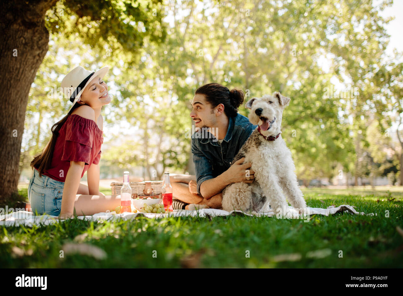 Giovane uomo accarezza un cane con donna seduta da presso il parco della città. Giovane avendo divertimento su pic-nic. Foto Stock