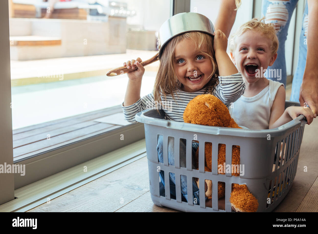 Emozionato i bambini seduti in un cestello di lavaggio essendo spinto dalla madre. Ragazza che indossa una ciotola come casco con ragazzo di ridere. Foto Stock