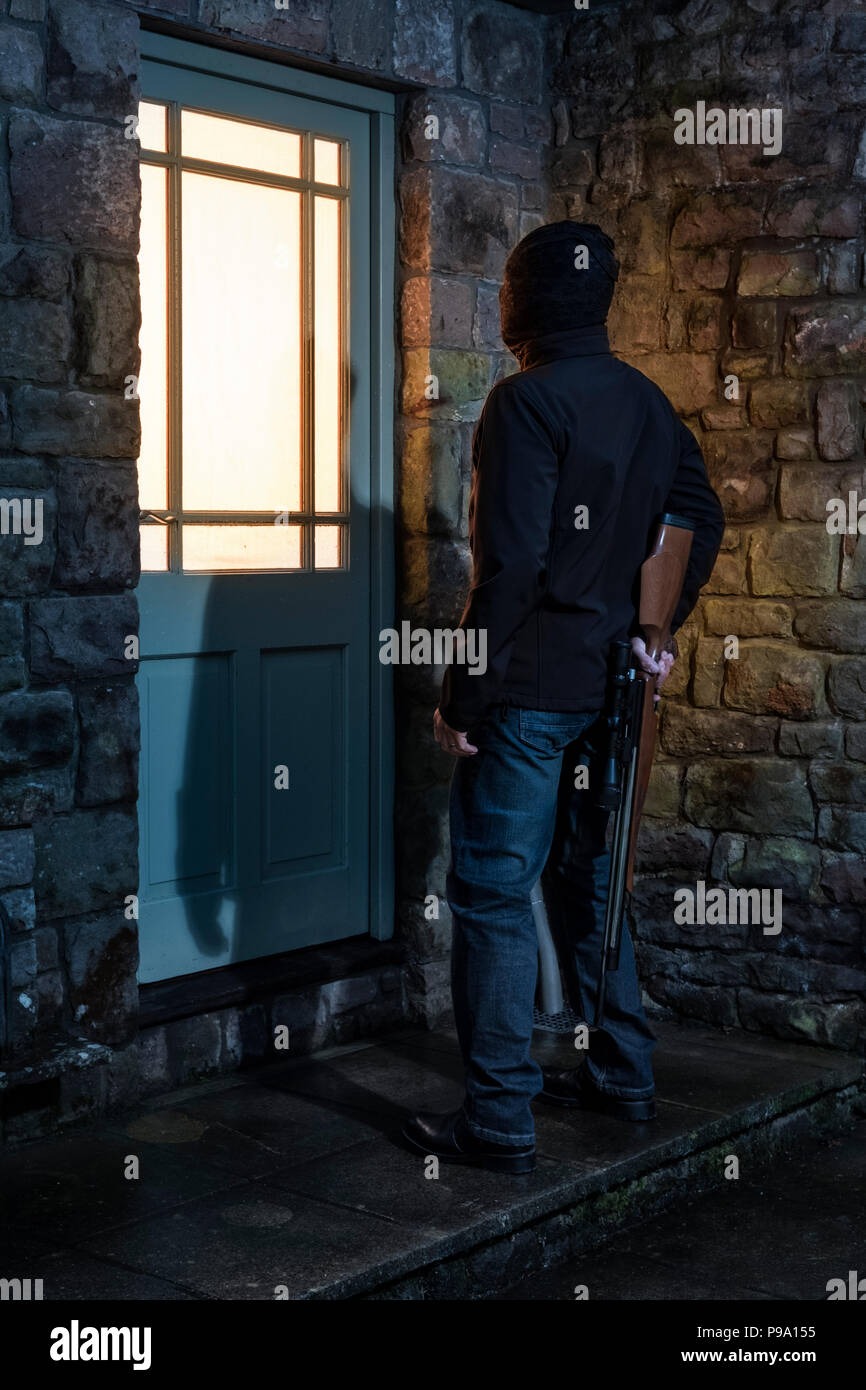 Un uomo con un fucile al di fuori di una porta di casa. Foto Stock