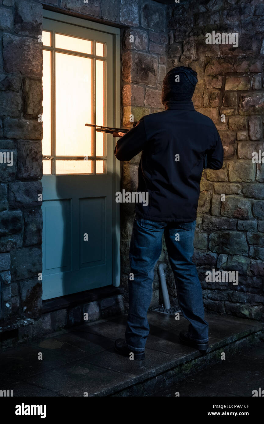 Un uomo con un fucile puntato su una porta di casa. Foto Stock