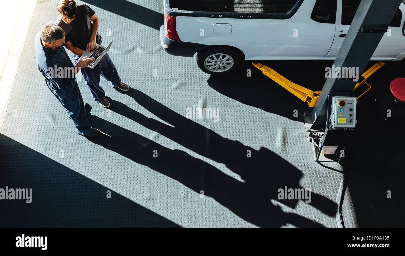 Vista dall'alto di due meccanici in piedi in officina per auto e di lavoro sul computer portatile. Professional meccanici che lavorano in auto di servizio di riparazione. Foto Stock