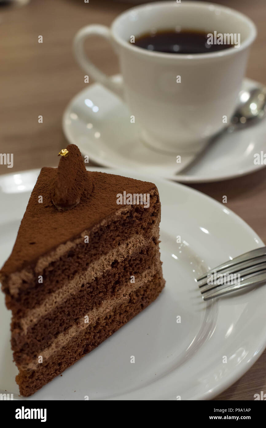 Torta al cioccolato con commestibili oro su piastra bianca con forcella e la tazza di caffè in background in base a una tabella. Foto Stock