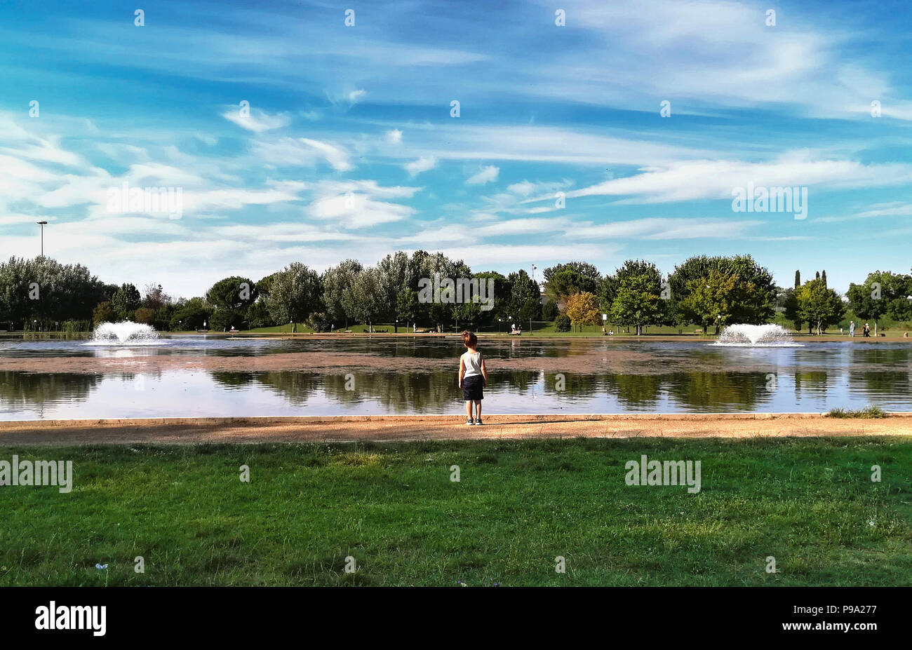 Bambino vista posteriore guardando tranquillo lago della scena in ambiente urbano green park nella stagione primaverile Foto Stock