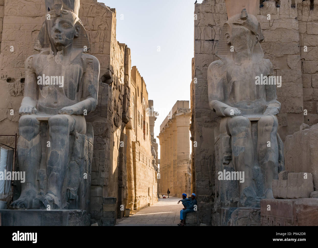 Seduto colossi figure di Ramses II al primo pilone entrata al Tempio di Luxor con locale guide egiziane in attesa per i turisti, Luxor, Egitto, Africa Foto Stock