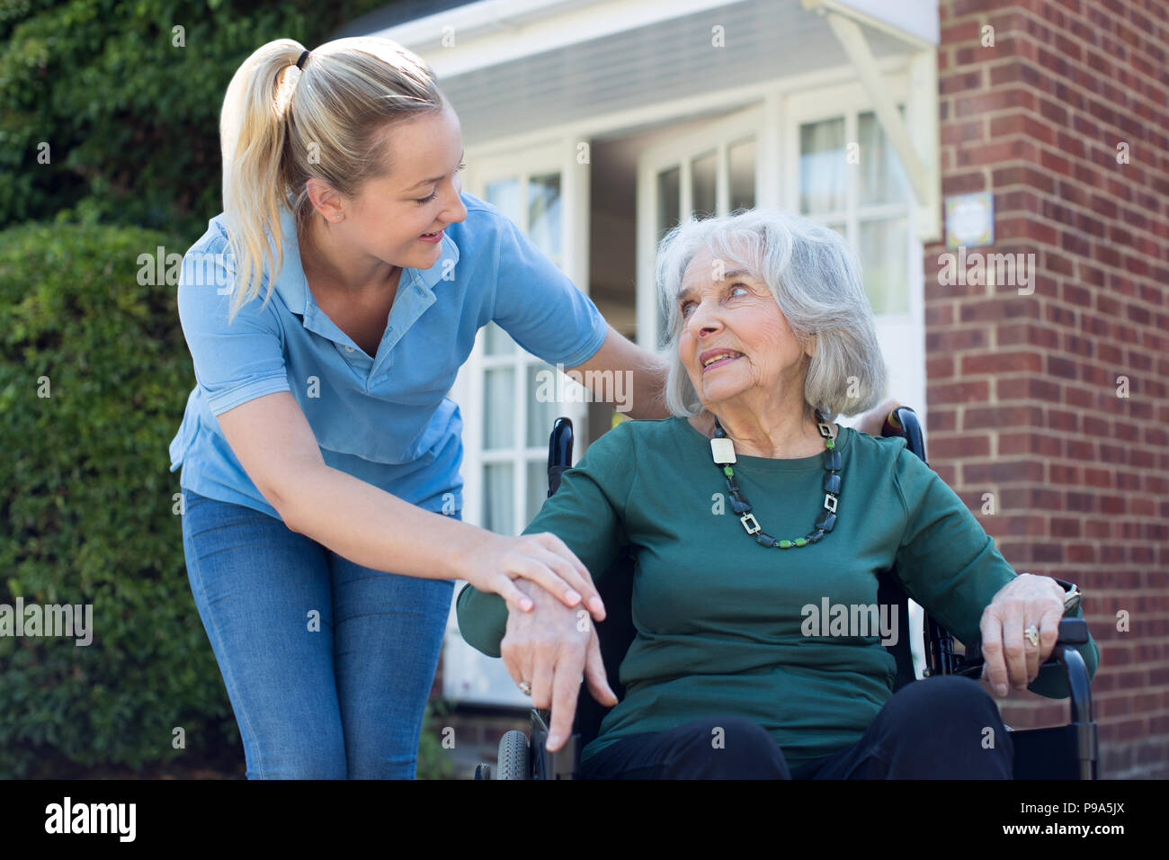 Accompagnatore spingendo Senior donna in carrozzella fuori casa Foto Stock