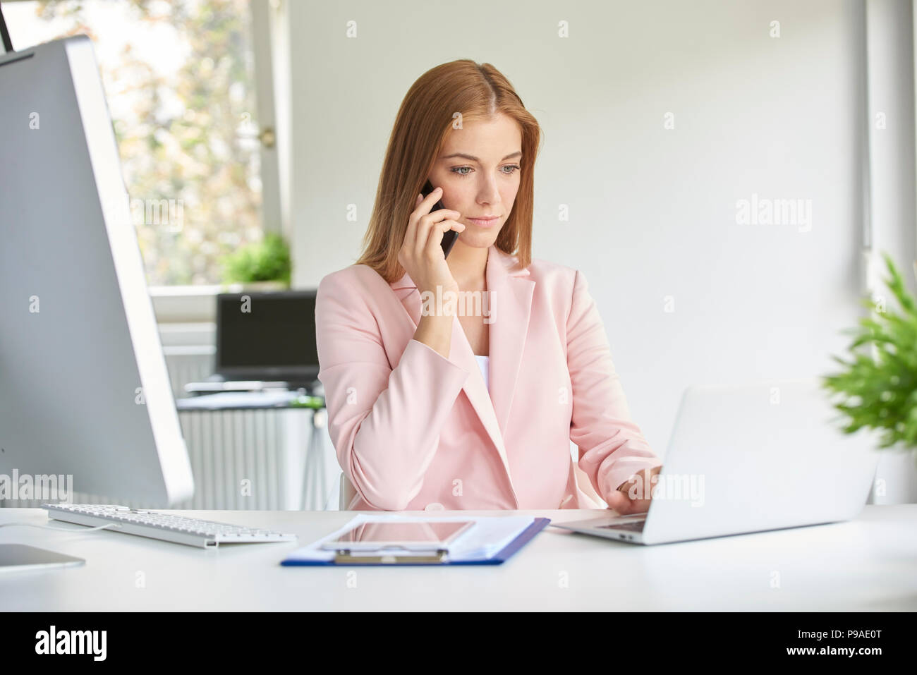 Attraente giovane imprenditrice di effettuazione della chiamata e utilizzando laptop mentre si lavora in un ufficio moderno. Foto Stock